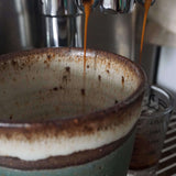 Brewing an espresso shot in handmade ceramic cup and measuring cup.