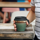 Woman using a matte green stoneware ceramic cup with silicone cover for her takeaway coffee.